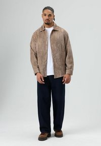 Brown corduroy button-up shirt with a relaxed fit, layered over a white t-shirt, paired with dark blue wide-leg pants and brown shoes.