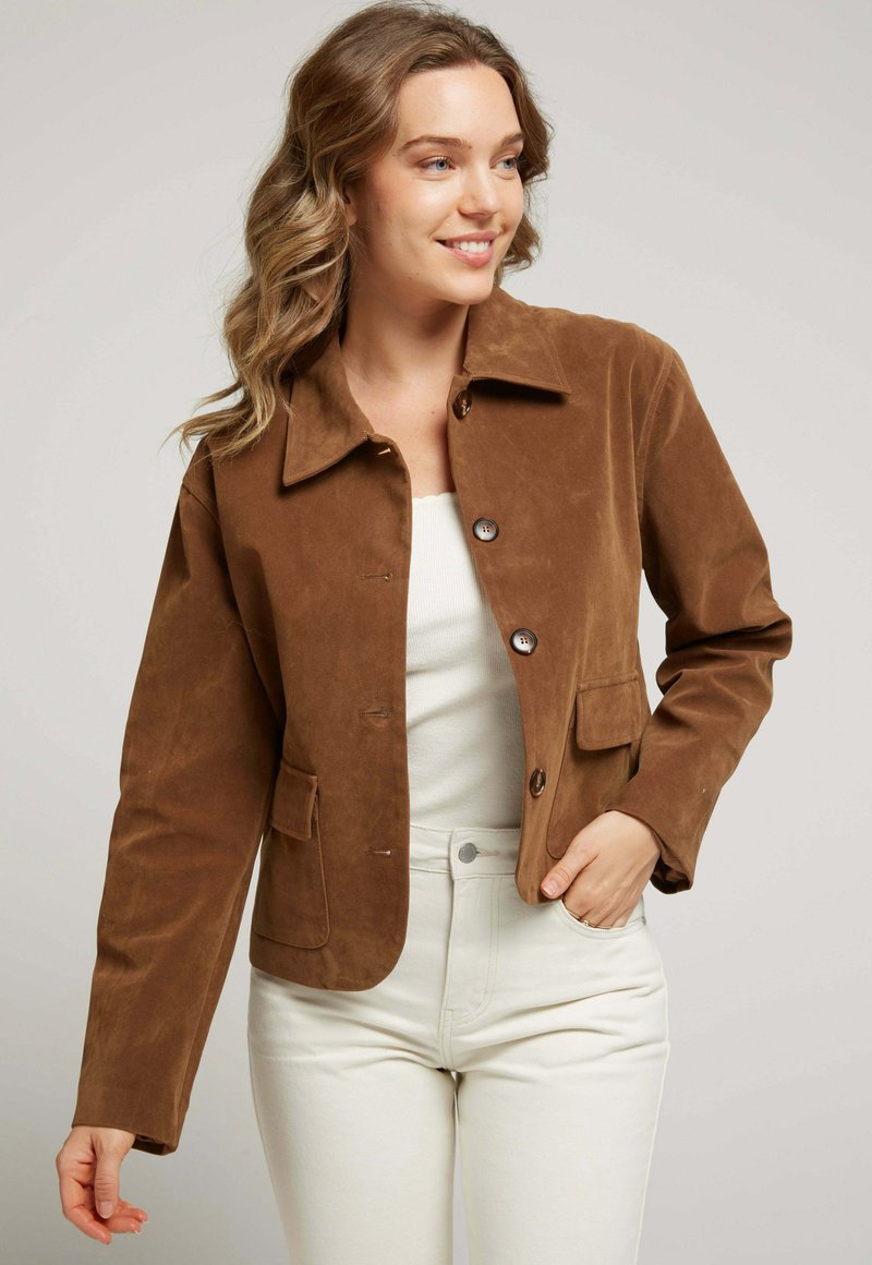 Veste en daim marron avec un col, deux poches avant et des fermetures à bouton. Présente une texture douce et un design ajusté.