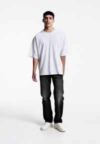 Bijela oversized pamučna majica, tamne uske traperice i bijele tenisice. Outfit se ističe opuštenim siluetom i jednostavnim dizajnom.