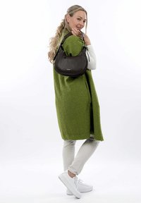 Sac à main en cuir marron foncé, de forme arrondie, avec une surface texturée. Associé à un manteau en polaire vert et des baskets blanches.