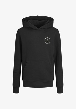 Personne portant un sweat à capuche noir avec poche avant et logo, pantalon cargo bleu marine et baskets blanches, debout devant un fond clair uni.