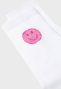 White cotton socks featuring a pink smiley face logo on the front. The fabric has a ribbed texture and a standard crew length.