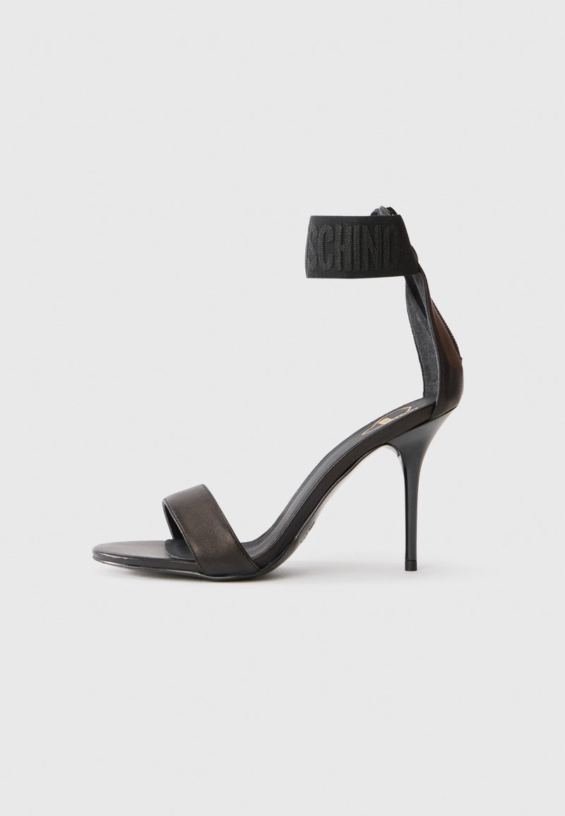 Μαύρη στυλέτο σανδάλι με λείο δέρμα επάνω, δύο φαρδιές ρίγες και επώνυμη μαυρη υφασμάτινη ταινία αστραγάλου. Διαθέτει κομψό σχέδιο με μυτερή μύτη.