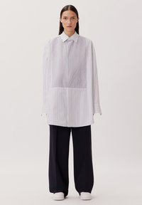 Camicia a righe bianca e blu navy, vestibilità oversize, maniche lunghe, colletto a punte, con un pannello testurizzato sul davanti e sul retro.