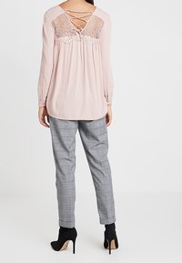 Blusa rosa a maniche lunghe con dettagli in pizzo sulla schiena, abbinata a pantaloni grigi a quadri e stivaletti neri. Fit sartoriale e rilassato.