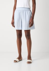Lichtblauwe shorts met verticale strepen, elastische tailleband en een relaxte pasvorm. Draagt met beige slidesandalen. Gladde stoftextuur.