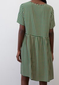 Vestido verde de manga corta con un patrón de cuadrícula en beige. El diseño presenta una falda acampanada y un escote redondo. Textura de tela suave.