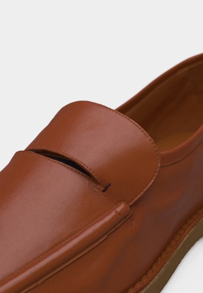 Mocassin à enfiler en cuir marron avec un petit talon et un détail de bride penny sur le dessus.