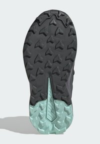 Black textured rubber outsole with prominent traction lugs; light mint green accents at center and heel. Distinctive zigzag and geometric patterns.