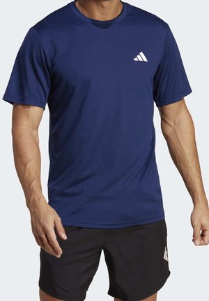 Homme portant un t-shirt Adidas bleu marine à manches courtes et un short Adidas noir avec des logos visibles sur la poitrine et la cuisse.