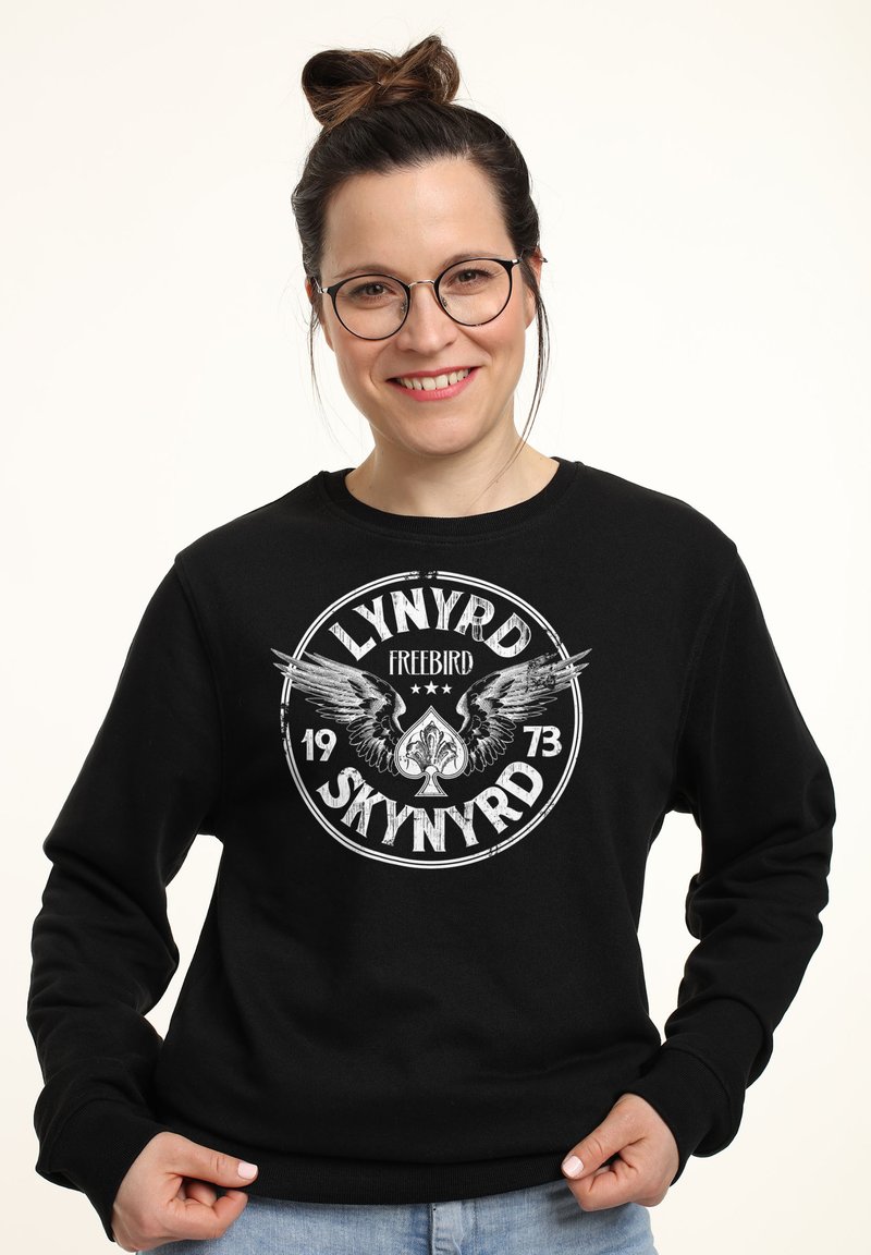 Felpa nera con un grafico circolare con il testo "LYNYRD SKYNYRD", ali e un design di asso di picche. Collo a giro e vestibilità casual.