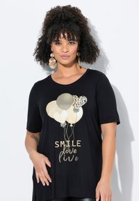 Černé tričko s krátkým rukávem, které má zlaté a vzorované balónkové motivy a text "SMILE love live". Vyrobeno z měkké látky s volným střihem.