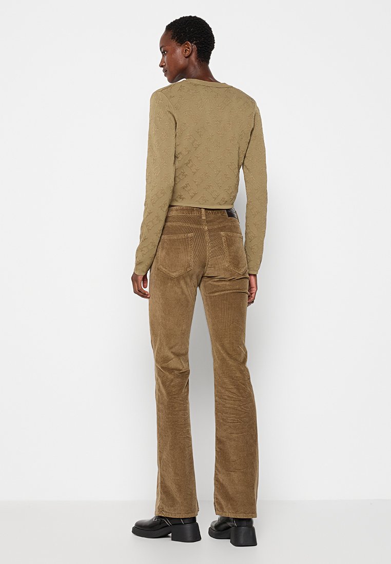 Oliwkowa, długosleeve bluzka z teksturowanym wzorem; brązowe, sztruksowe spodnie dzwony z tylnymi kieszeniami i wysokim stanem; czarne buty.