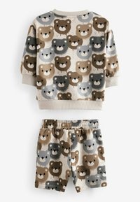 Beżowy zestaw składający się z bluzy i szortów, z wzorem przedstawiającym twarz misia w odcieniach brązu, szarości i czerni. Bluza ma prążkowane mankiety i dekolt.