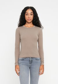 Langärmliges, Crew-Neck-Oberteil in Taubfarben, aus einem glatten Material gefertigt. Kombiniert mit eng anliegenden, hellblauen Jeans, die einfache Nähte aufweisen.