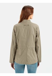 Let hver, beige jakke med ståkrave og indsnøret talje; har knaplukket epauletter og lange ærmer.
