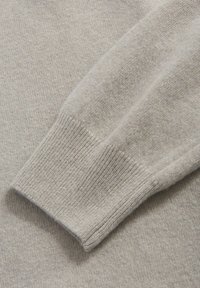 Hellgraues Pulloverdetail mit einem gerippten Bündchen und weicher Textur, mit einem insgesamt glatten Strickmuster und dezenten Schattierungsvariationen.