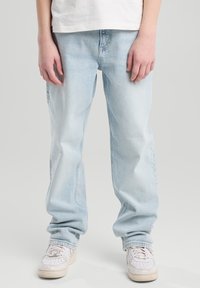 Vaaleansiniset denim-farkut, joissa on rento malli, näkyvillä ompeluominaisuuksilla ja joustavilla lahkeilla. Yhdistetty valkoisiin tennareihin.