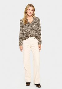 Blouse à imprimé léopard avec des manches longues, un col et des poignets élastiques, associée à un pantalon large crème taille haute et des chaussures marron.