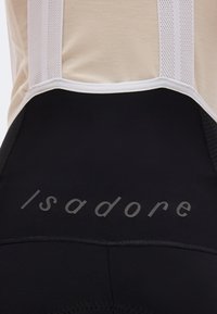 Κοντινή λήψη μαύρων ποδηλατικών σορτς με λευκές ζώνες από δίχτυ και ανακλαστικό λογότυπο «Isadore» στο κάτω μέρος της πλάτης.