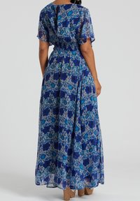 Blue floral maxi dress with short flutter sleeves, smocked waist, and an open back detail. Made of lightweight, flowy fabric.