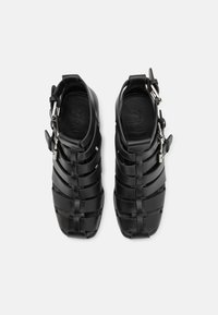 Svarte, snøre sandaler med vevd design. Laget av glatt materiale, med en side spenne og åpen hæl. Teksturert fotseng.