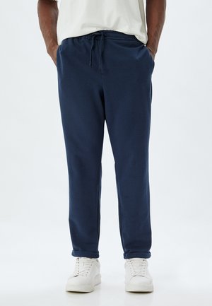 Mørkeblå sweatpants lavet af blødt stof, med en elastisk talje og snor samt sidelommer. Stylet med hvide sneakers.