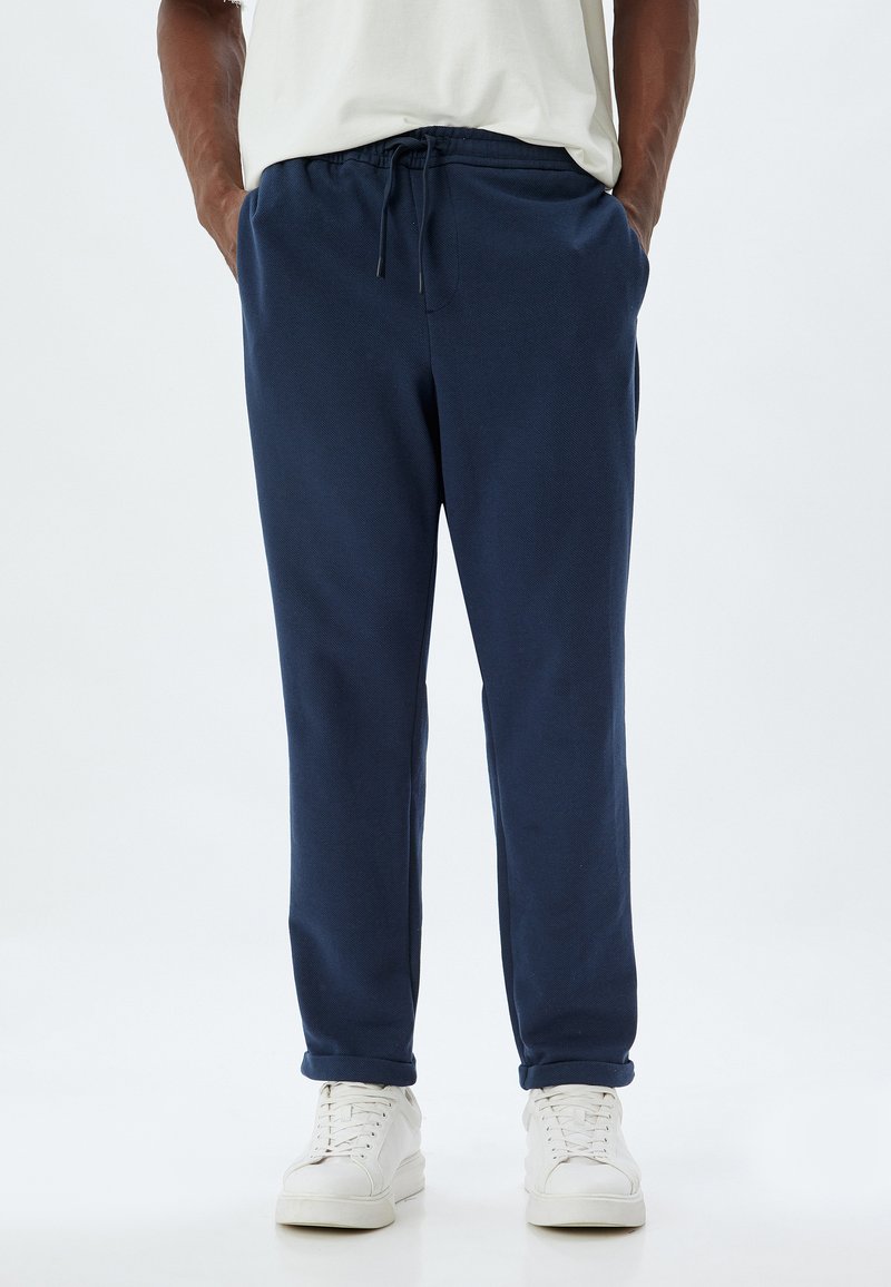 Mørkeblå sweatpants lavet af blødt stof, med en elastisk talje og snor samt sidelommer. Stylet med hvide sneakers.