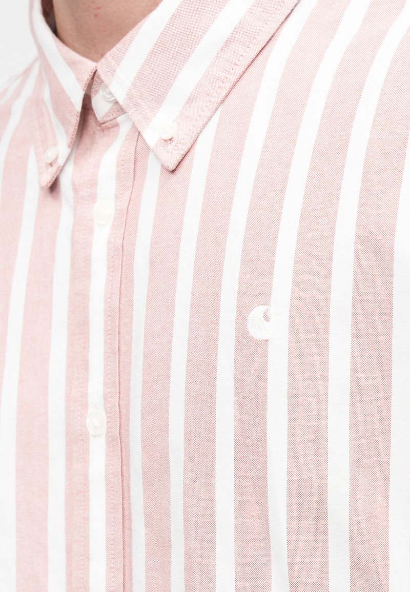 Chemise à rayures rose clair et blanches en tissu texturé, avec un col et un petit logo sur le côté gauche.