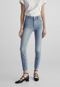 Lichtblauwe skinny jeans met een hoge taille, lichte stretch en voorzakken. Gecombineerd met een witte t-shirt met opgerolde mouwen en zwarte ballerina's.