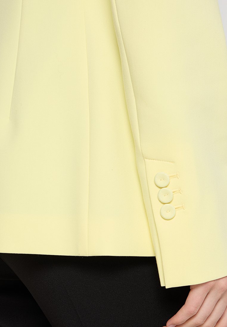 Gelber maßgeschneiderter Blazer mit strukturierten Schulterpartien, glattem Stoff und einem Detail mit vier Knöpfen an den Ärmeln. Schlanker Schnitt mit einer seitlichen Tasche.