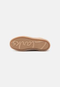 Tan sneaker sål med en struktureret gummioverflade, der har spor og et fremtrædende logo i kursiv henover midten.
