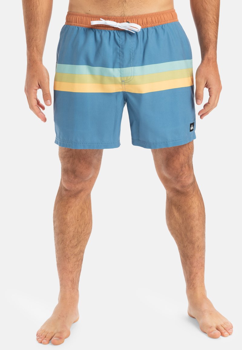Bañador azul hecho de tejido ligero, con rayas horizontales en azul claro, verde y amarillo. Cintura elástica con cordón ajustable.