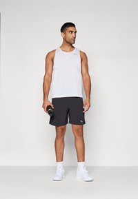Hvid atletisk tanktop med mesh-struktur, sorte shorts og hvide sneakers. Holder en sort vandflaske, enkelt design og PUMA-logo synligt.