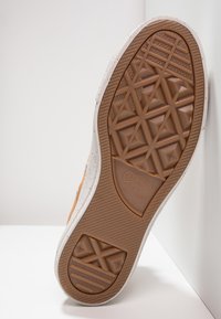Light brown rubber sole with patterned traction, featuring a white midsole. Upper detail in muted orange fabric with slight speckling.