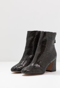 Botines de tobillo texturizados en negro con un brillante patrón de piel de serpiente, punteras afiladas y tacones cuadrados, diseñados para un ajuste ajustado.