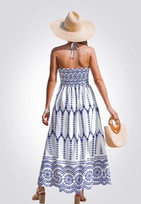 Vestido maxi sin tirantes de tela blanca con un patrón floral azul. Combinado con un bolso de paja tejido y un sombrero de paja.