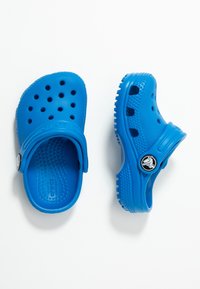 Pár modrých Crocs kopyt s ventilačními otvory, nastavitelnými popruhy na patě a texturovanými podrážkami na bílém pozadí.