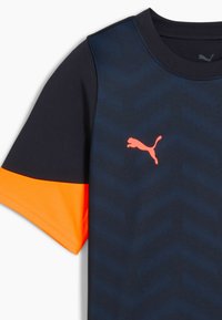 Camiseta deportiva negra y naranja con un panel superior texturizado, que presenta un prominente logo de Puma en rosa en el pecho y mangas cortas.