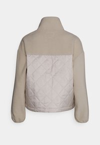 Beige fleecejacka med ett quiltat, ljusbeige bakpanel, hög krage och vida ärmar med elastisk fåll.
