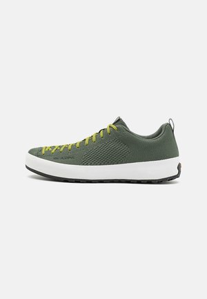 Baskets basses avec dessus en mesh respirant vert foncé, lacets jaunes, semelle épaisse blanche et semelle extérieure noire, vues de côté.