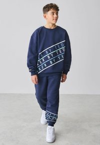 Marineblauer Sweatshirt- und Hosenset mit weißen und türkisen Textstreifen. Weicher Stoff mit lockerem Sitz, akzentuiert durch gerippte Bündchen an Ärmeln und Knöcheln.