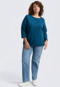 Teal blue top with a round neckline and three-quarter sleeves, paired with light blue straight-leg jeans and white sneakers.