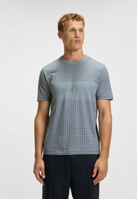 Ljusblå T-shirt med kort ärm och rutmönster, med en logotyp på framsidan och rundad halsringning. Slät textur.