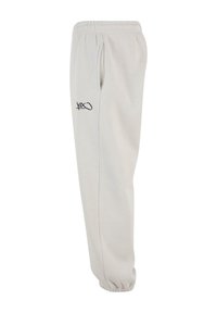 Lys grå sweatpants med elastisk talje, sidelommer og et sort logo trykt på venstre lår. Ribkanter ved anklerne. Blød tekstur.