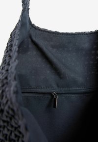 Černá tkaná taška s texturovaným vnějším povrchem, s hladkým vnitřním materiálem a zipovou kapsou pro bezpečné uložení.