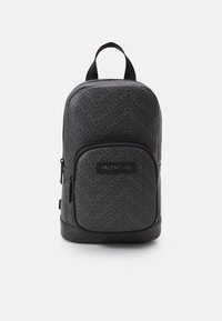 Black leather backpack with repeating "Valentino" logo pattern, zippered front pocket, and top handle for carrying. Smooth texture, compact design.