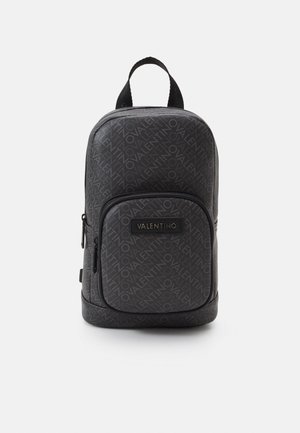 Musta nahkainen reppu, jossa toistuva "Valentino"-logokuvio, vetoketjuinen etutasku ja kantokahva yläosassa. Sileä pinta, kompakti muotoilu.