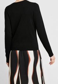 Svart långärmad tröja med rund halsringning och ribbad nederkant. Bärs med en mönstrad kjol i svarta, vita och bruna nyanser.