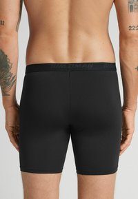 Pantalones cortos deportivos negros fabricados con un tejido elástico, que cuentan con una cinturilla estrecha con el nombre de la marca impreso de manera sutil. Textura suave y diseño ajustado.